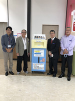 返却ポストを囲んで撮影に応じる、知花教育長、泉川図書館長等四名の代表の写真