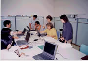 白い机にノートパソコンが数台置かれており、パソコンを動かす人と教えている人が集まって作業している農業簿記講座の様子を撮った写真