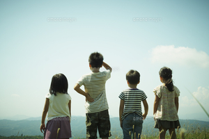 子どもたちが4人並んで、遠くの空と山を眺めている様子を背中側から撮影した写真