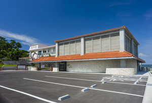 オレンジ色の屋根と白い柱で2階建の博物館全体と、手前の駐車場が見える写真