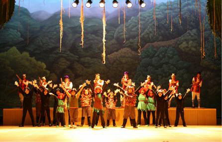 さまざまな衣装に身を包み両手を上に挙げている人たちが舞台上で所狭しと並んでいる鳳ホールで行われた創作子どもミュージカルの様子を撮影した写真