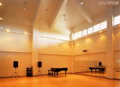 ピアノやアンプとスピーカーが設置されている鳳ホールのリハーサル室の写真