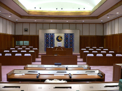 中央列に筆記机が並び、両壁際に講義用の机と椅子が並んでいる会議室の写真