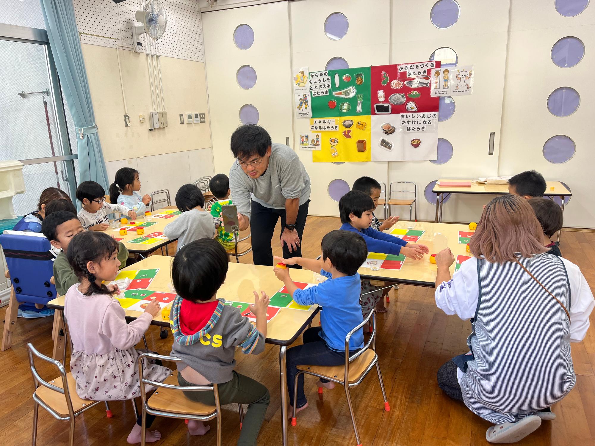 子どもたちに「食育」のお話をしている先生と机に座って話を聞く園児たちの写真